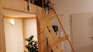 Eine Holztreppe mit einem Sessel und einem Blumentopf in einem Raum mit Holzdielen und weißen Wänden.