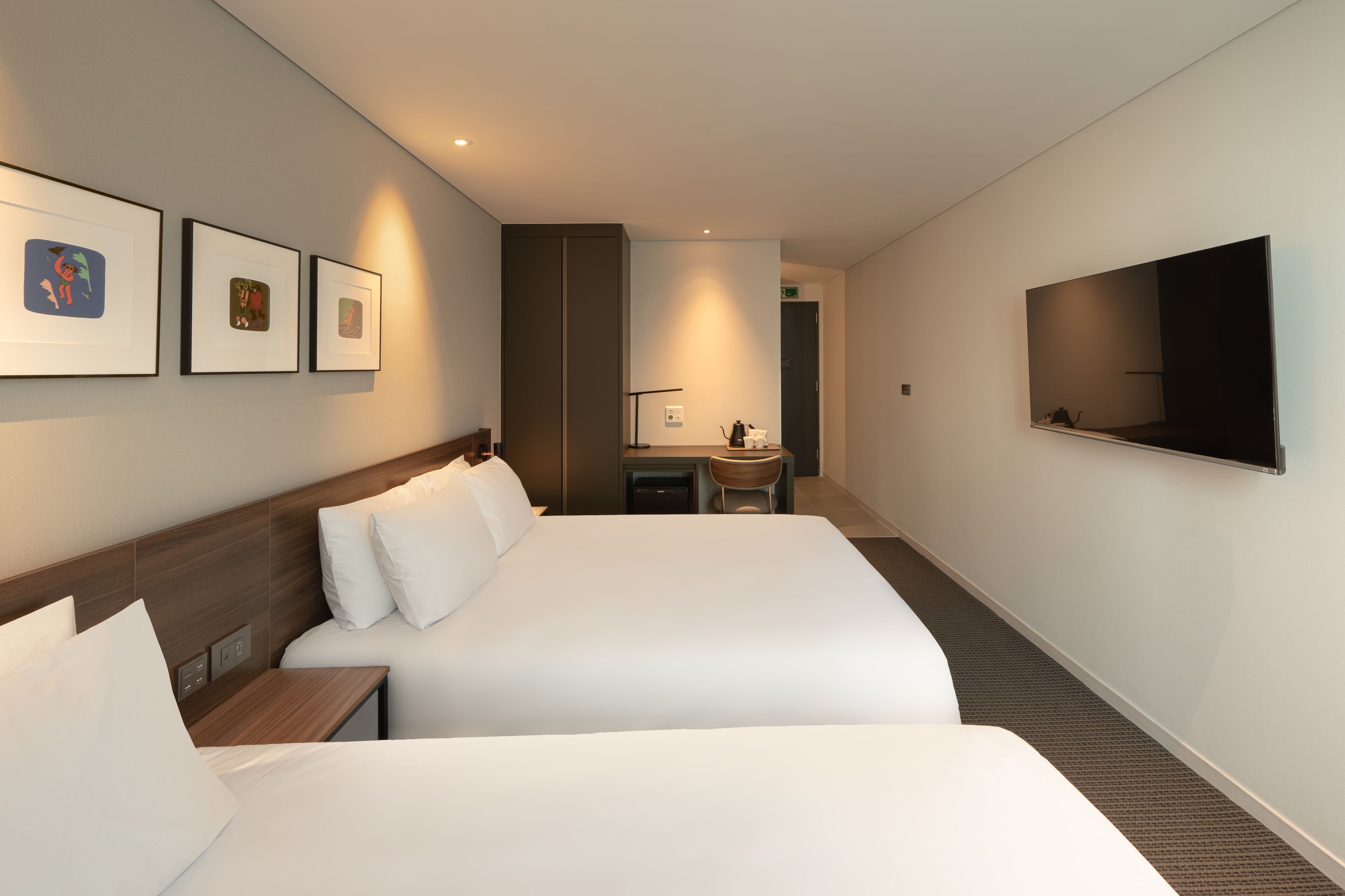 A hotel room with two beds, a flat-screen TV, a desk with a chair, and framed artwork on the wall.