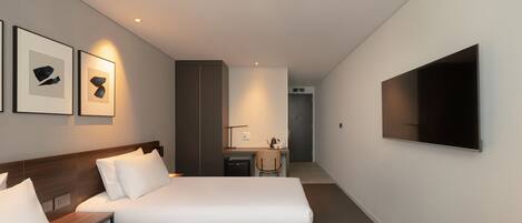 Quarto de hotel com duas camas, uma escrivaninha, uma cadeira, televisão e obras de arte na parede.