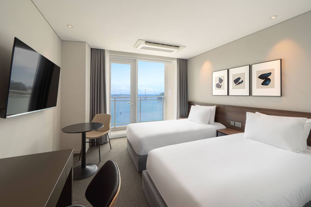 A hotel room with two beds, a TV, a small table, and a chair.