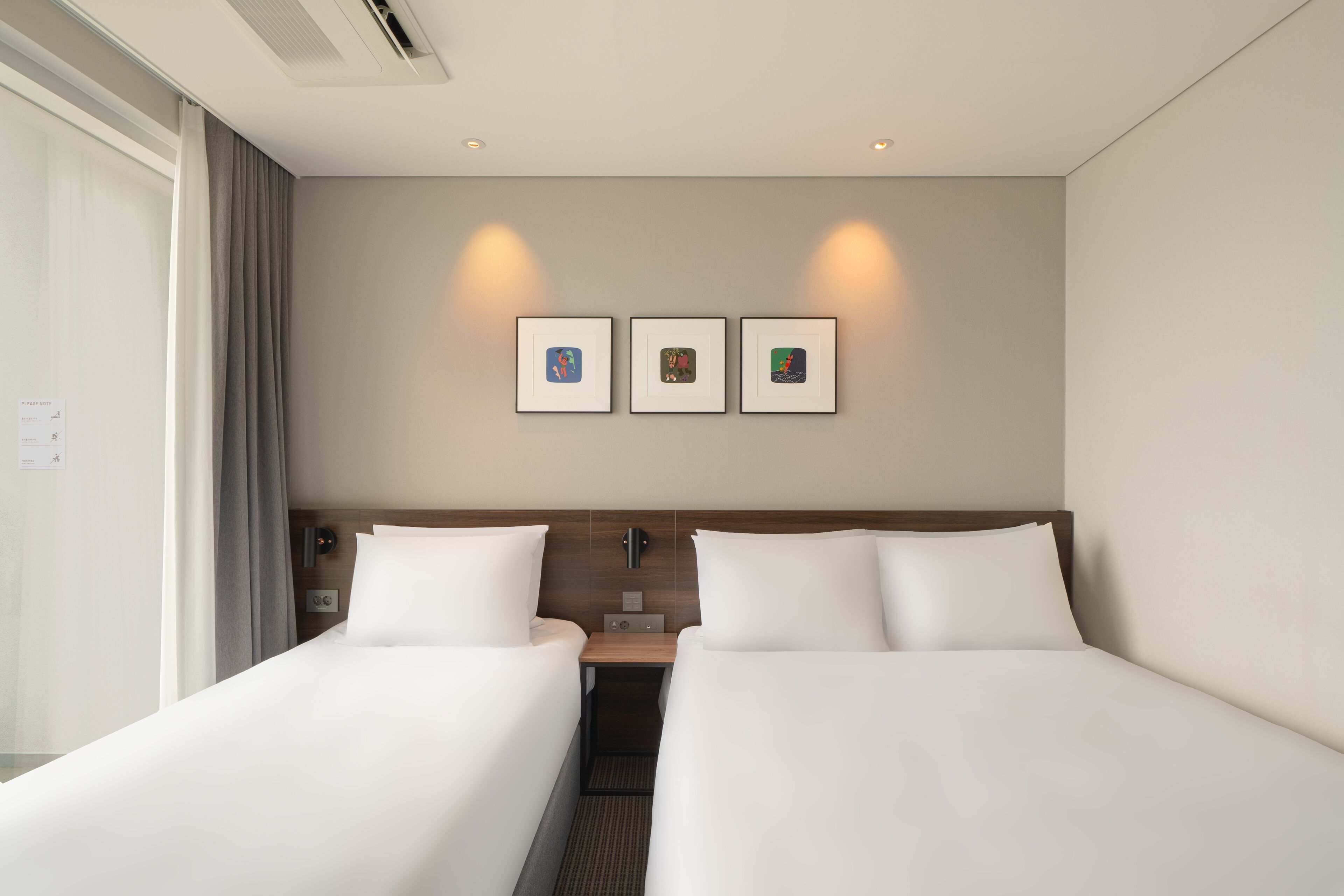 Une chambre d’hôtel avec deux lits, une table de chevet, une lampe et trois tableaux encadrés au mur.