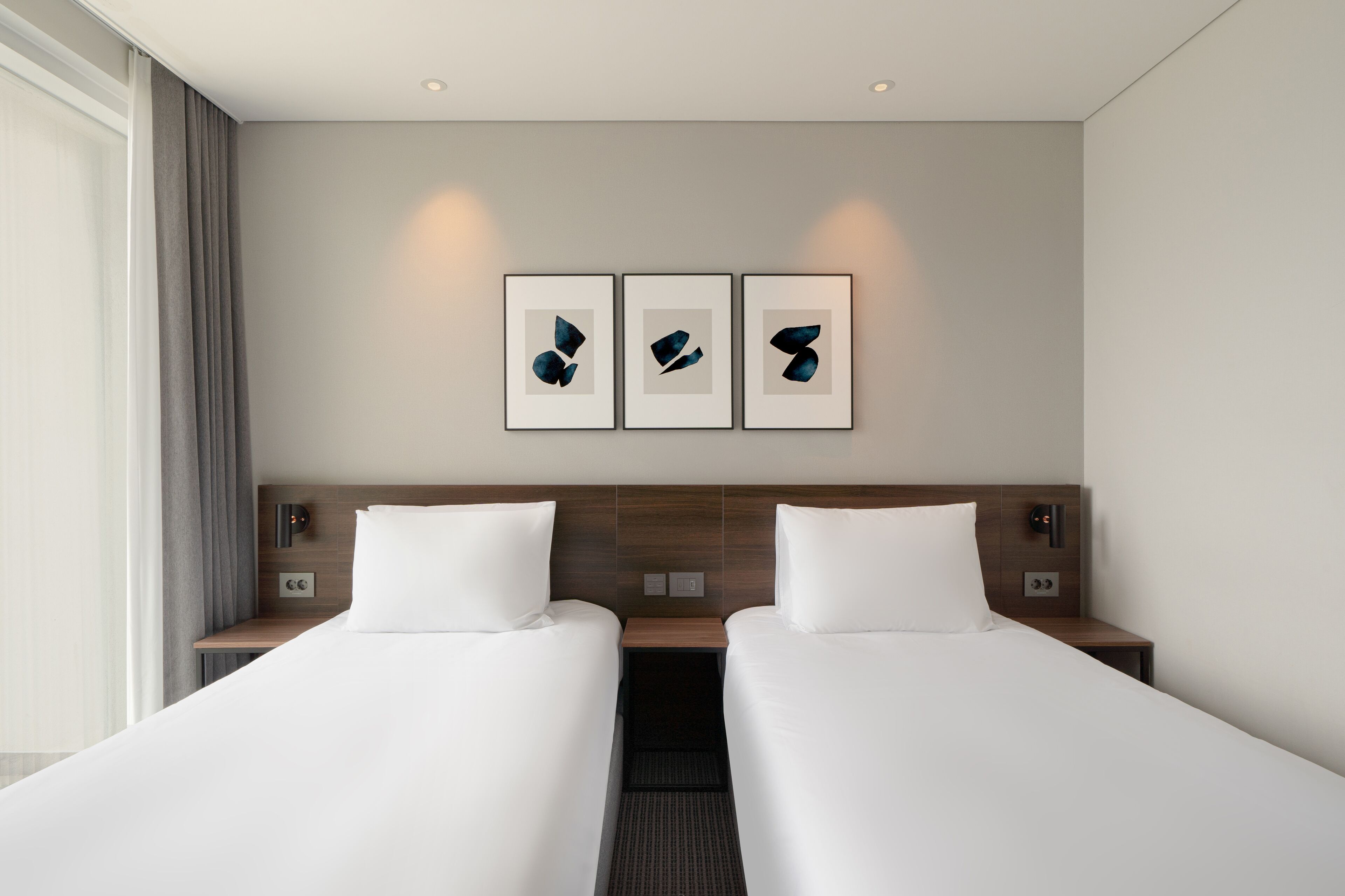 Ein Hotelzimmer mit zwei Betten, einem hölzernen Kopfteil, Nachttischen und drei gerahmten abstrakten Kunstwerken an der Wand.