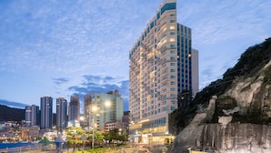 A high-rise hotel with multiple floors, a well-lit entrance, and a view of surrounding buildings and natural rock formations.