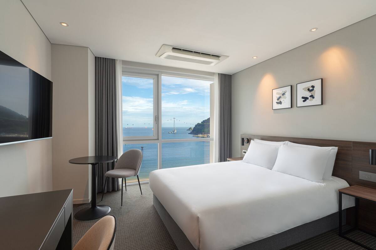 A hotel room with a large bed, a desk, a chair, and a view of the sea.
