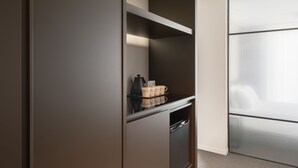 A modern, minimalist kitchenette with a built-in oven, a coffee maker, and a kettle.