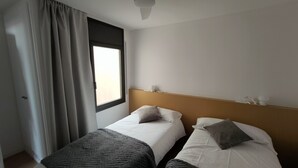 Habitación de hotel con dos camas, una ventana con cortinas, una pared lisa y una lámpara en el techo.