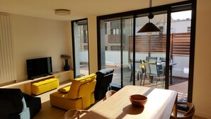 Una sala de estar moderna con televisor, sofá amarillo y un comedor con mesa y sillas.
