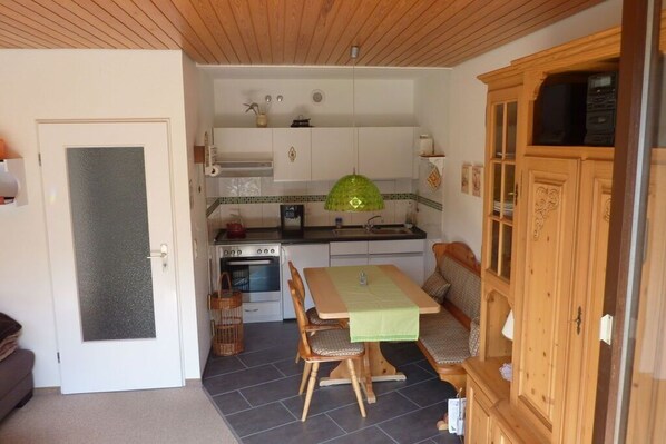 A compact kitchen with a dining area, wooden cabinets, and a green hanging light fixture.