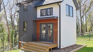 A modern two-story house with a wooden deck, a dark grey exterior, and a white upper section.