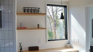 A modern kitchen with built-in shelves, a window with a view of trees, and a pendant light.
