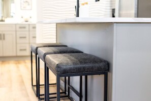 A modern kitchen with white cabinets, a marble countertop, and two black bar stools.