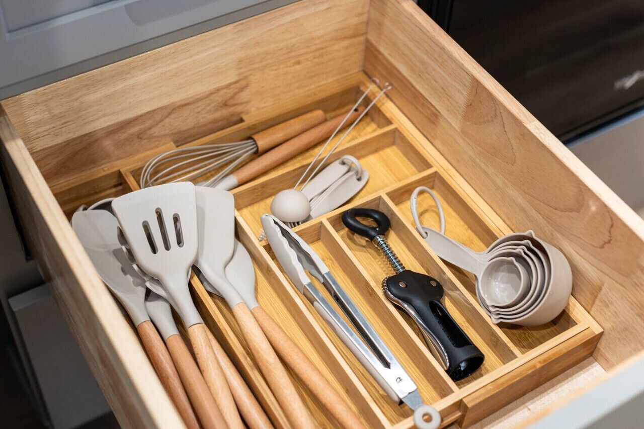 Un tiroir en bois contenant des ustensiles de cuisine, notamment des spatules, des fouets, une râpe et un verre doseur.