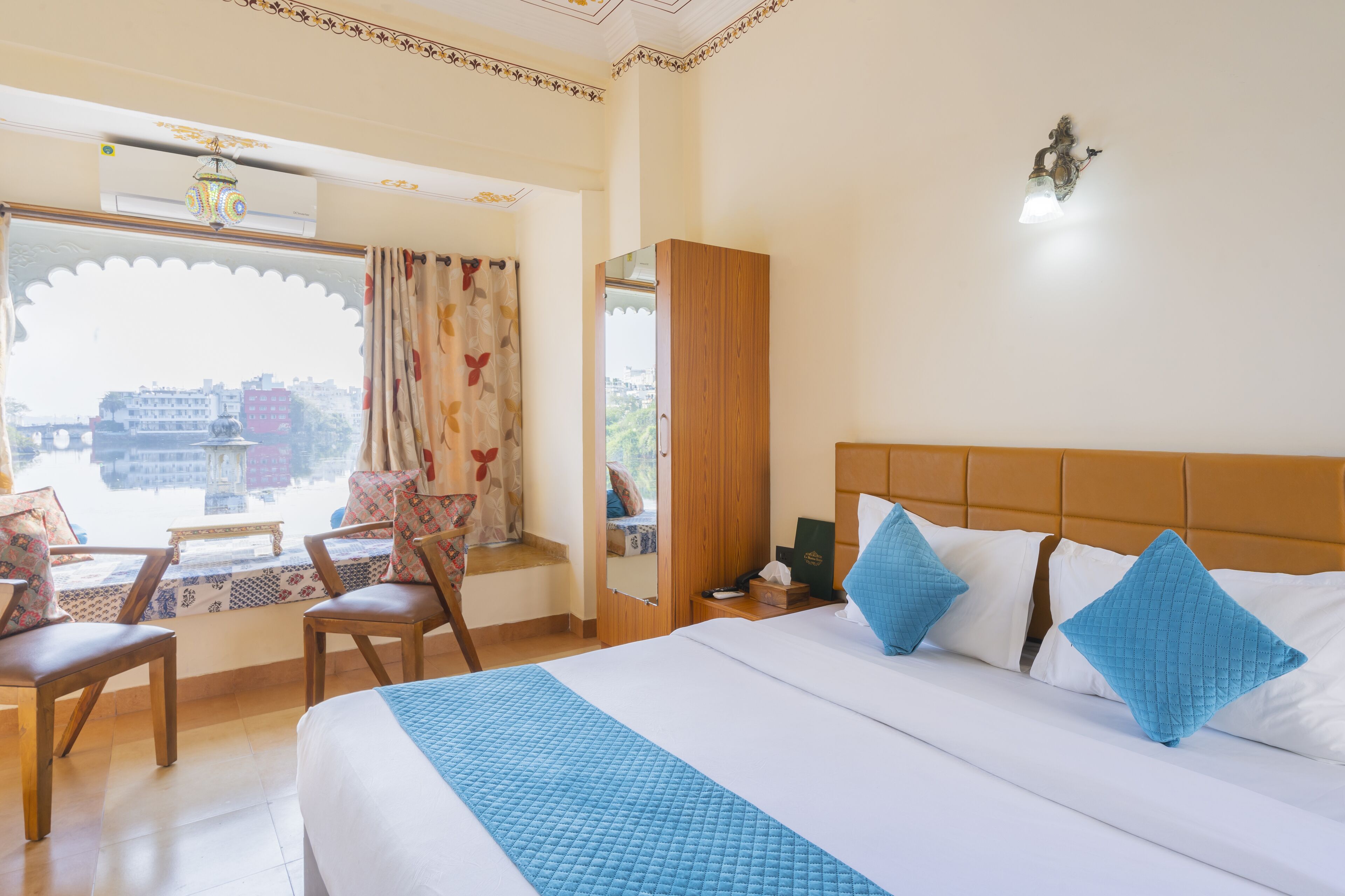 A hotel room with a large bed, a window with curtains, a wooden wardrobe, and a small table with chairs.