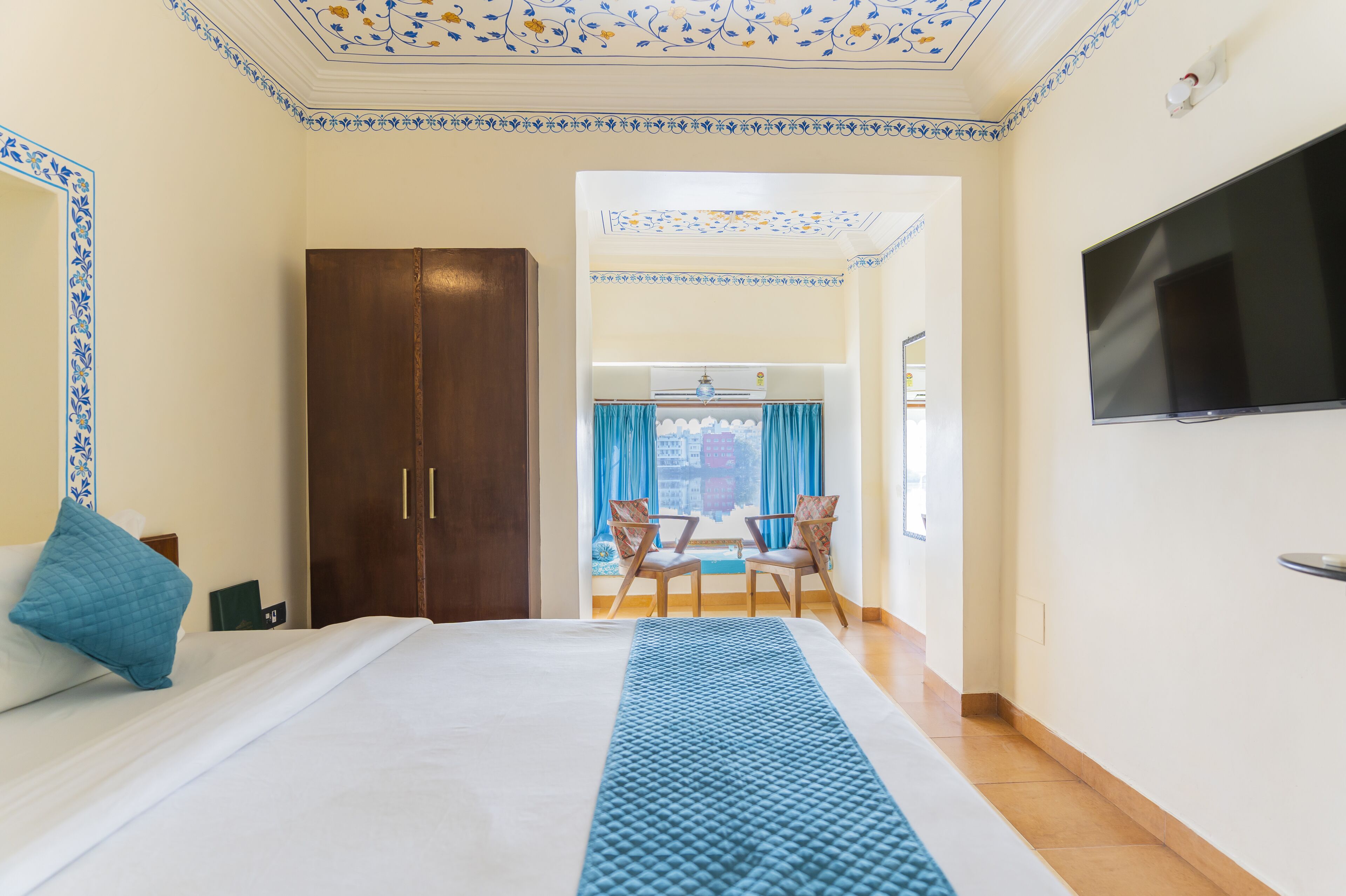 Une chambre d’hôtel avec un grand lit, un téléviseur fixé au mur et une vue sur la ville par la fenêtre.