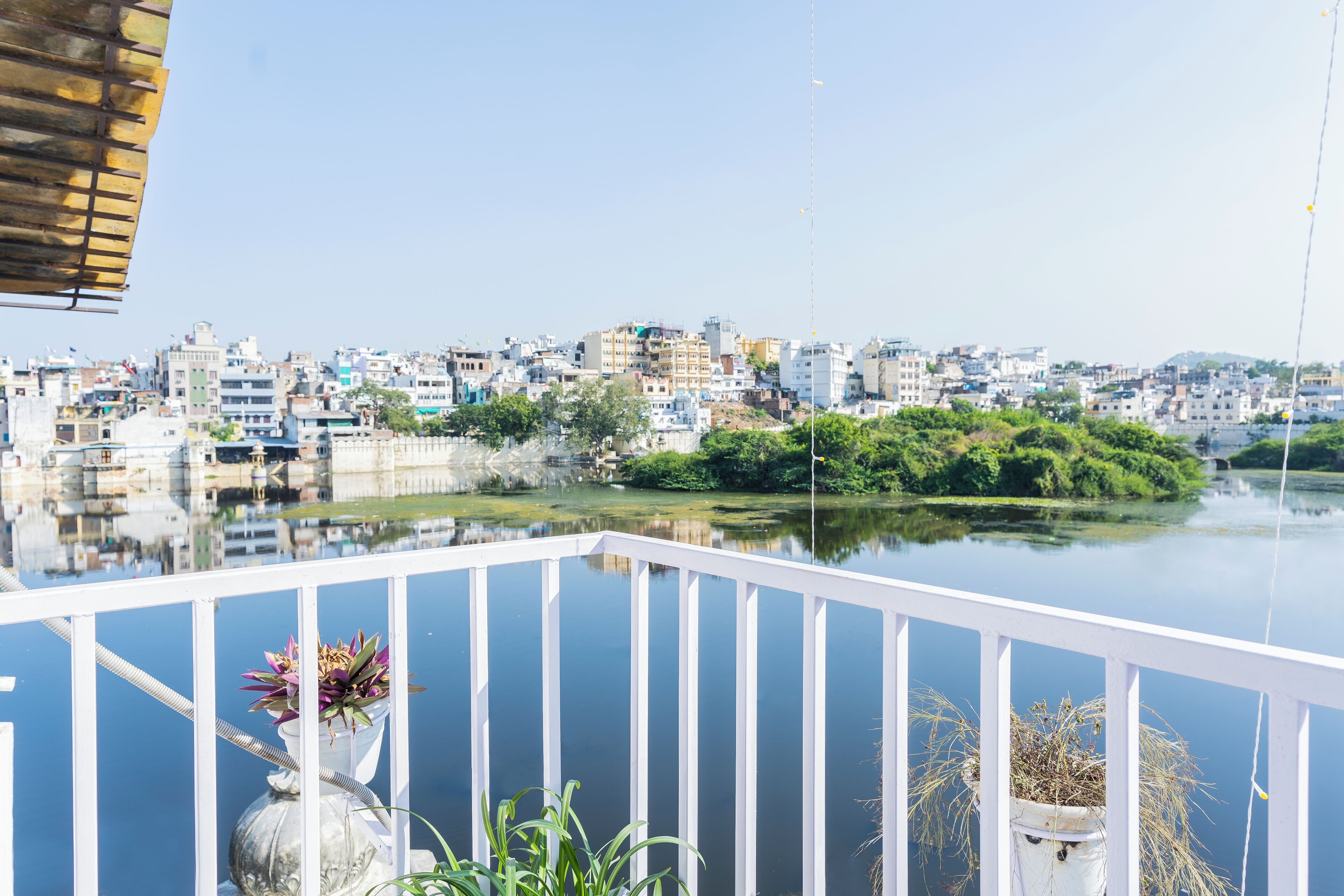 A balcony with white railings overlooking a cityscape with buildings and a river.
