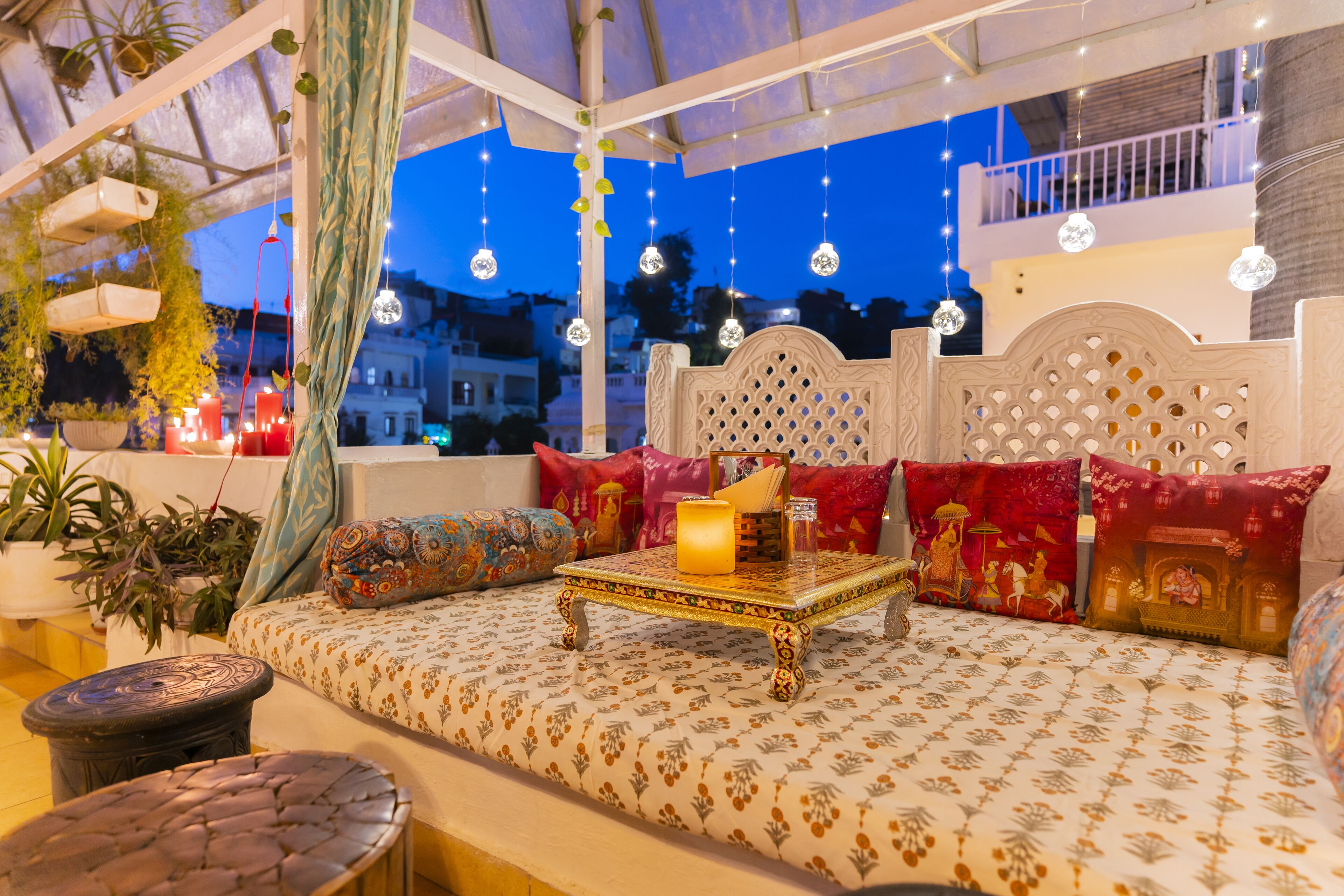 Un rincón exterior acogedor con un sofá estampado, una mesa decorativa y luces colgantes.