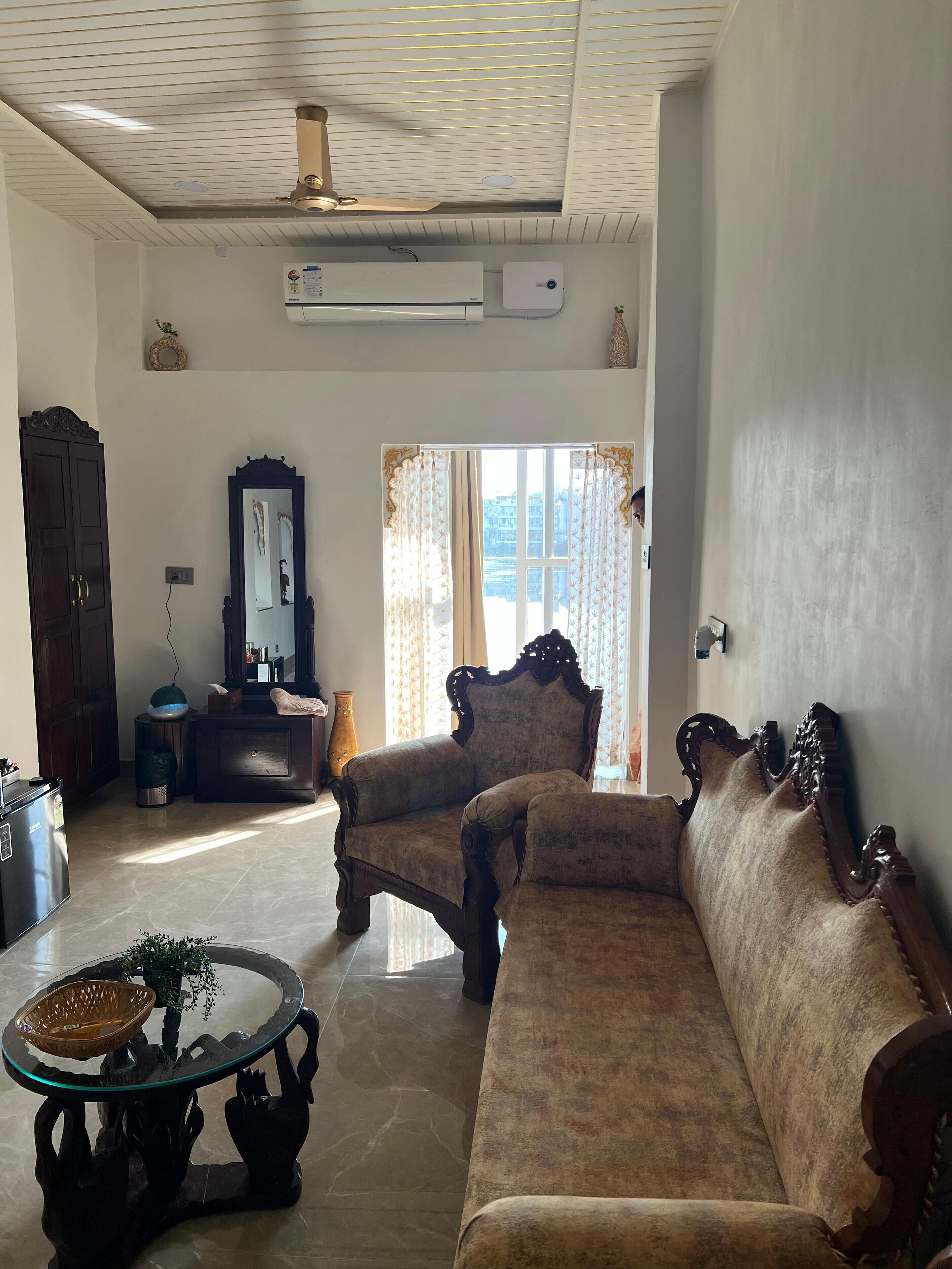 A living room with a sofa, armchairs, a glass coffee table, a mirror, and a ceiling fan.