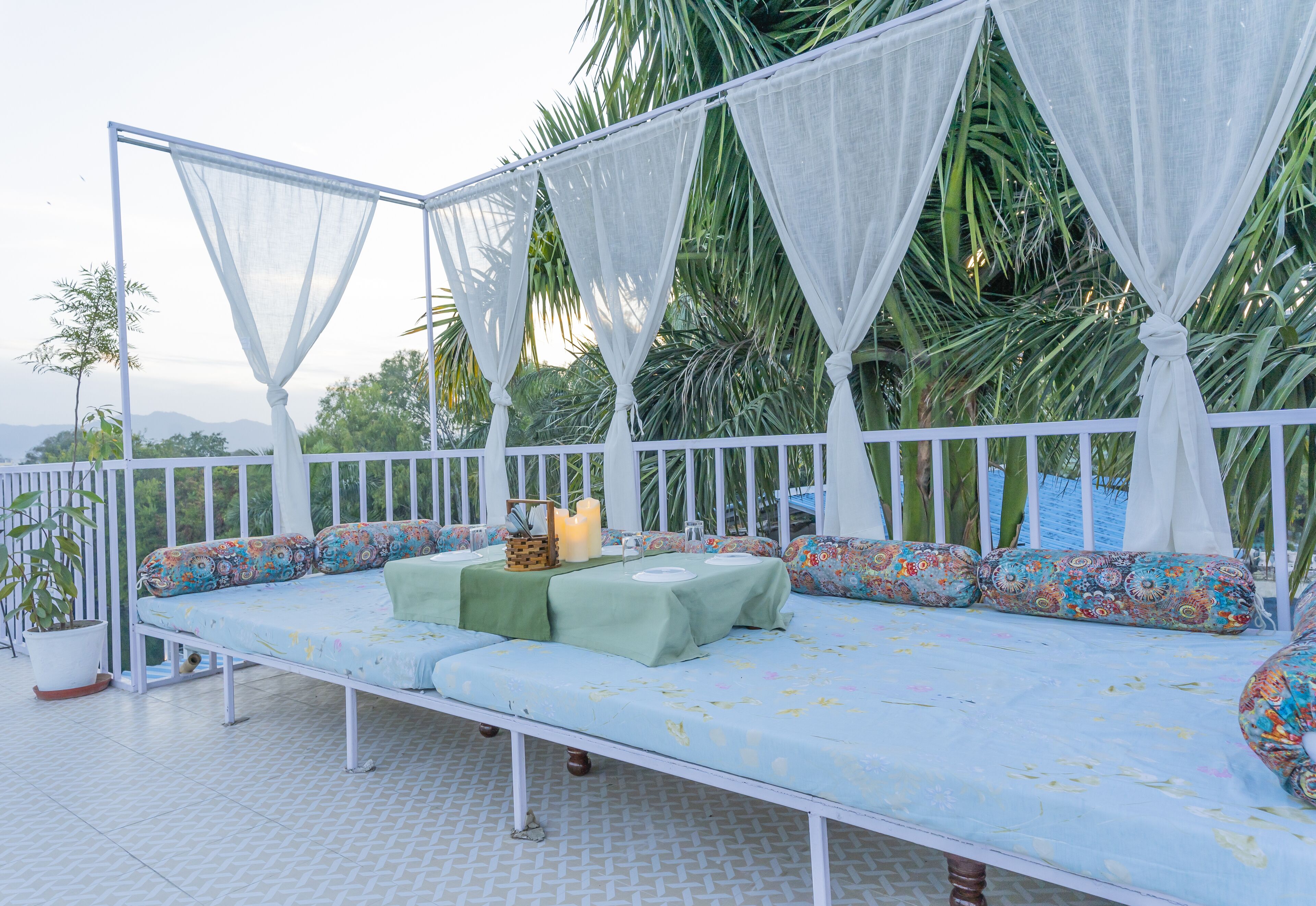 A balcony with a bed, a table with candles, and a potted plant.