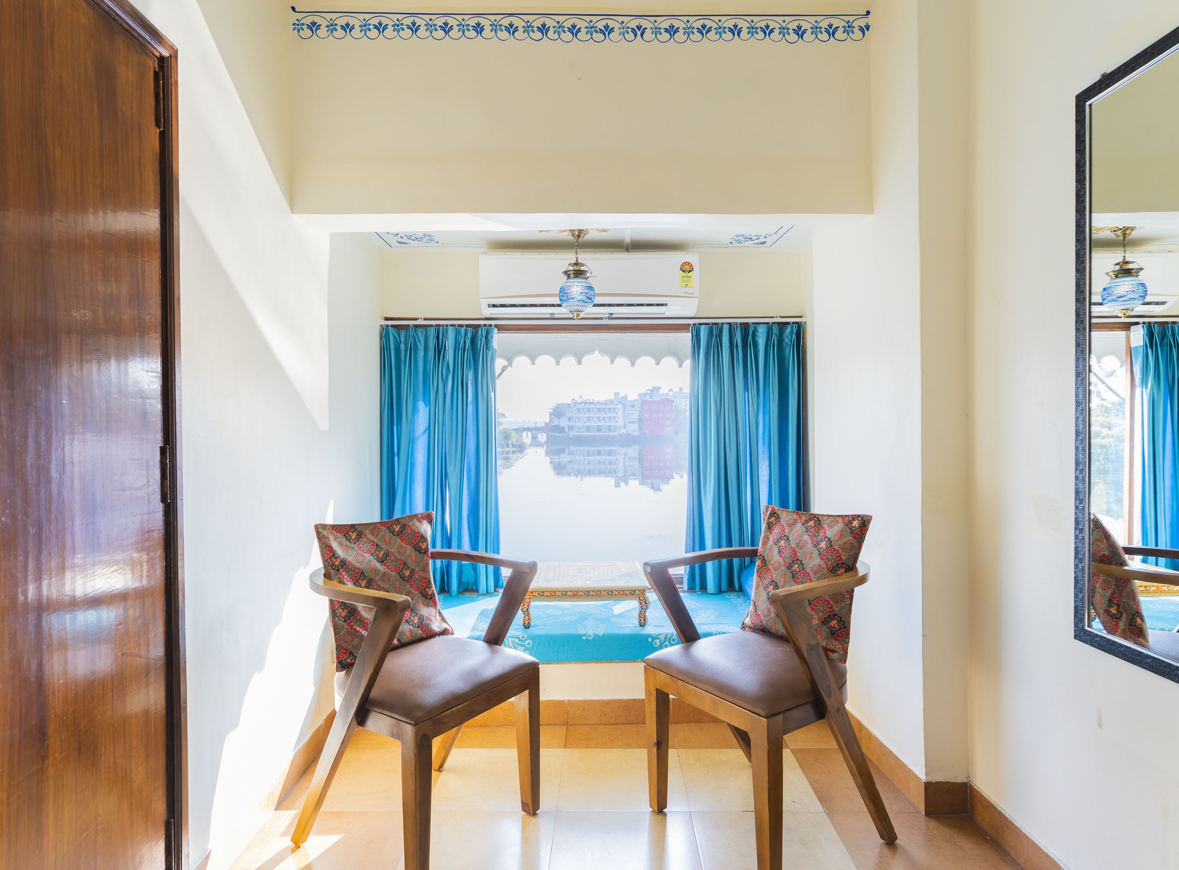 A room with two wooden chairs, a ceiling fan, and a view of a cityscape through blue curtains.