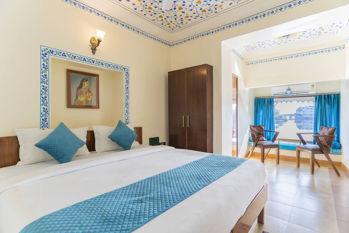 A hotel room with a large bed, a wardrobe, a painting on the wall, and a balcony with chairs.