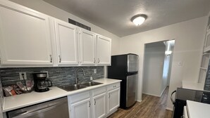 A modern kitchen with white cabinets, stainless steel appliances, and a wood floor.
