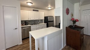 A compact kitchen with white cabinets, a stainless steel refrigerator, and a wooden island.