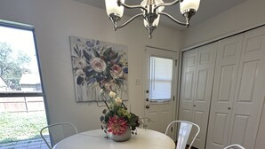 A dining area with a round table, white chairs, a chandelier, a floral painting, and a sliding door.