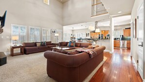A spacious living room with a large brown sectional sofa, a dining area, and a kitchen in the background. - Scenic Serenity in Immaculate Custom Home with Breathtaking Mountain Views & Cozy Fireplace (Boise)