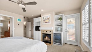 A bedroom with a bed, a fireplace, a ceiling fan, and a door with blinds. - Scenic Serenity in Immaculate Custom Home with Breathtaking Mountain Views & Cozy Fireplace (Boise)