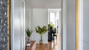 A hallway with wooden flooring, white walls, and a black bookshelf. There are two potted plants on a table. - Jervis Bay Sanctuary by Experience Jervis Bay (Vincentia)