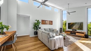 A spacious living area with a grey sofa, wooden coffee table, and a large flat-screen TV. - Jervis Bay Sanctuary by Experience Jervis Bay (Vincentia)