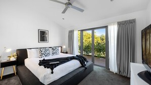 A modern bedroom with a large bed, a ceiling fan, a nightstand with a lamp, and a view of greenery through the window. - Jervis Bay Sanctuary by Experience Jervis Bay (Vincentia)