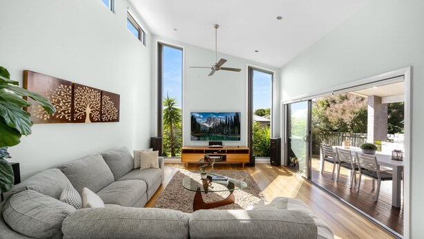 A spacious living room with a large flat-screen TV, a ceiling fan, and a sliding glass door leading to an outdoor patio. - Jervis Bay Sanctuary by Experience Jervis Bay (Vincentia)