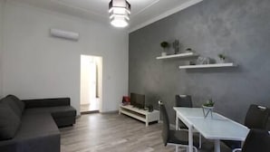 A modern living room with a grey sectional sofa, a white dining table with chairs, and a grey accent wall with shelves. - Tembo House - Pantano 2 (Catania)