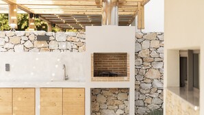 Una cocina exterior con pared de piedra, armarios de madera y horno de ladrillo.