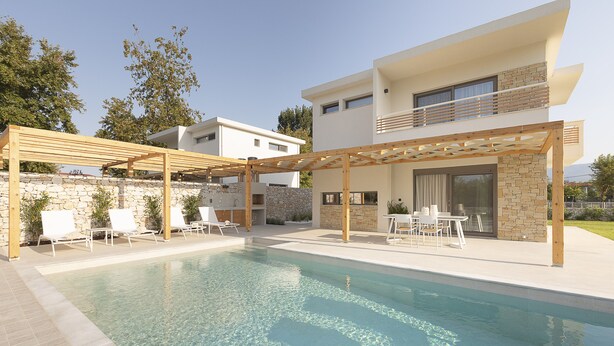 Un área de piscina moderna con una pérgola, sillones de descanso y un muro de piedra.