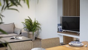 Una sala de estar moderna con sofá, una mesa de comedor con platos y cubiertos, un helecho en maceta y un televisor de pantalla plana.