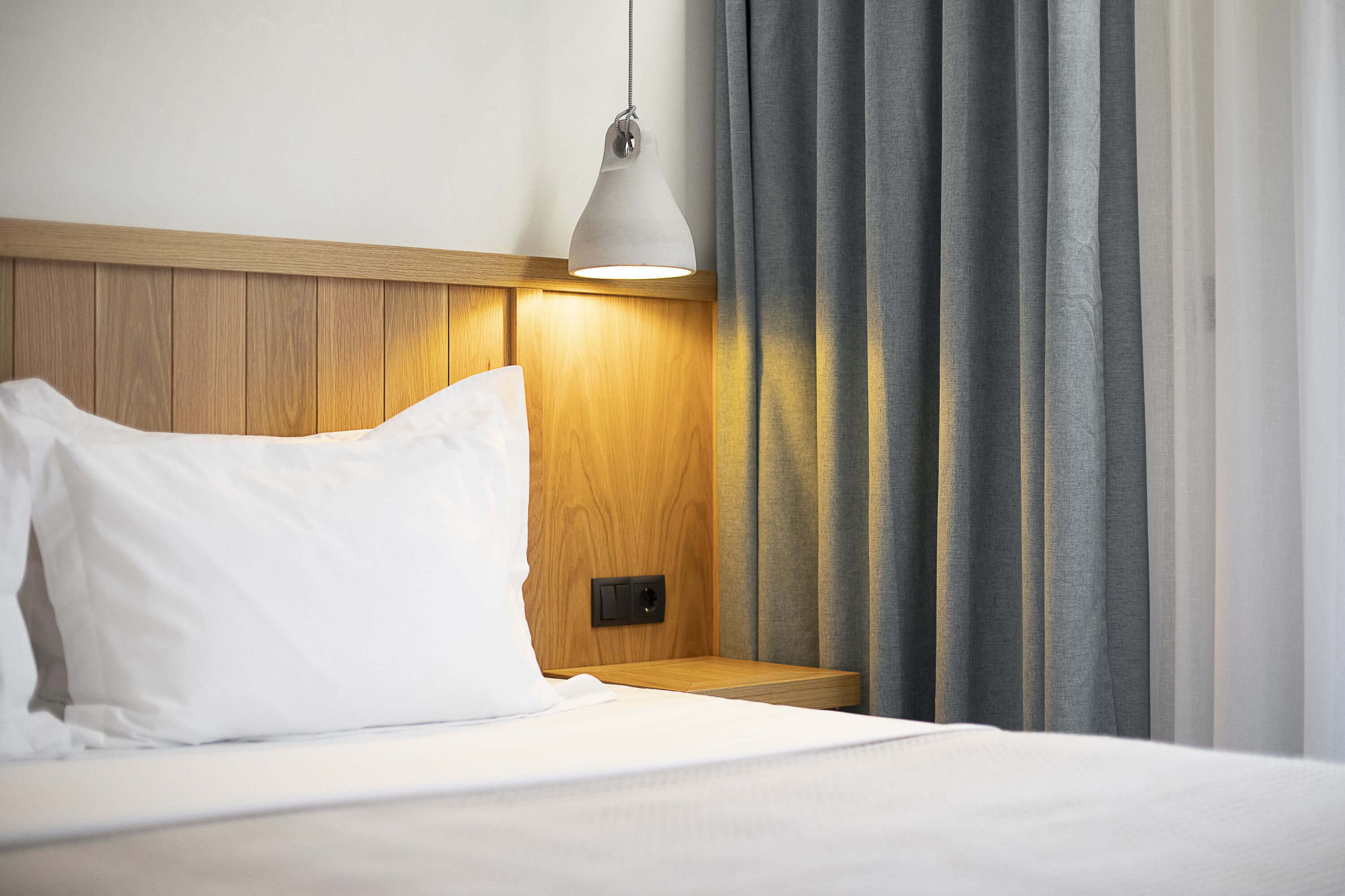 Een keurig opgemaakt bed met witte lakens, een houten hoofdbord en een bedlampje.