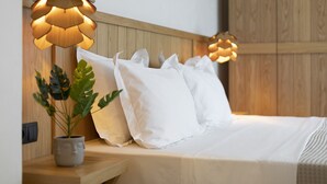 Una cama bien hecha con ropa de cama blanca, un cabecero de madera y una planta en maceta sobre la mesita de noche.