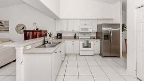 Une cuisine moderne avec des meubles blancs, des appareils en acier inoxydable et un sol carrelé.
