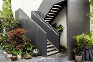 A modern staircase with a metal railing, surrounded by potted plants and a variety of foliage.