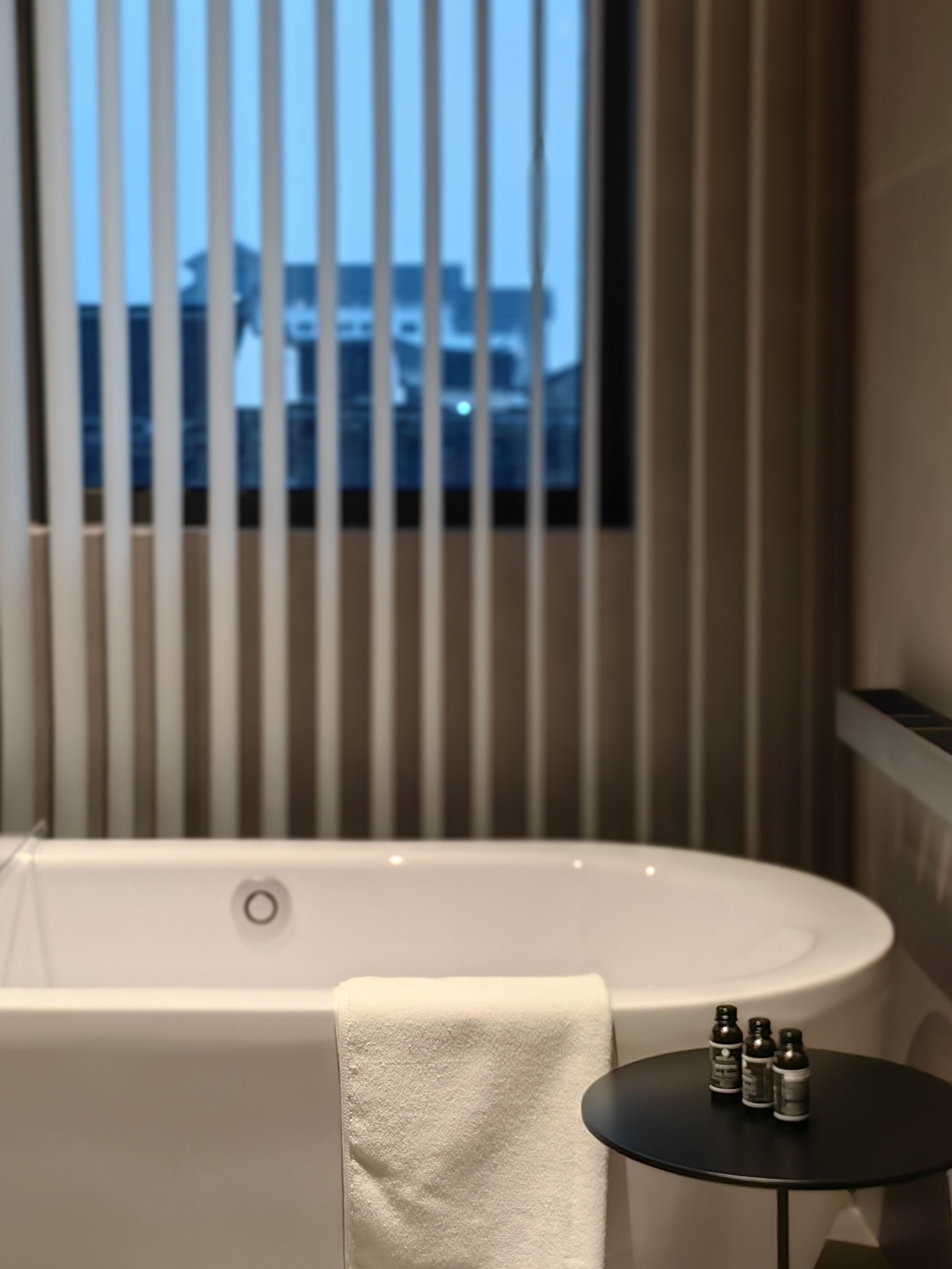 A modern bathroom with a bathtub, a towel, and a small table with toiletries.