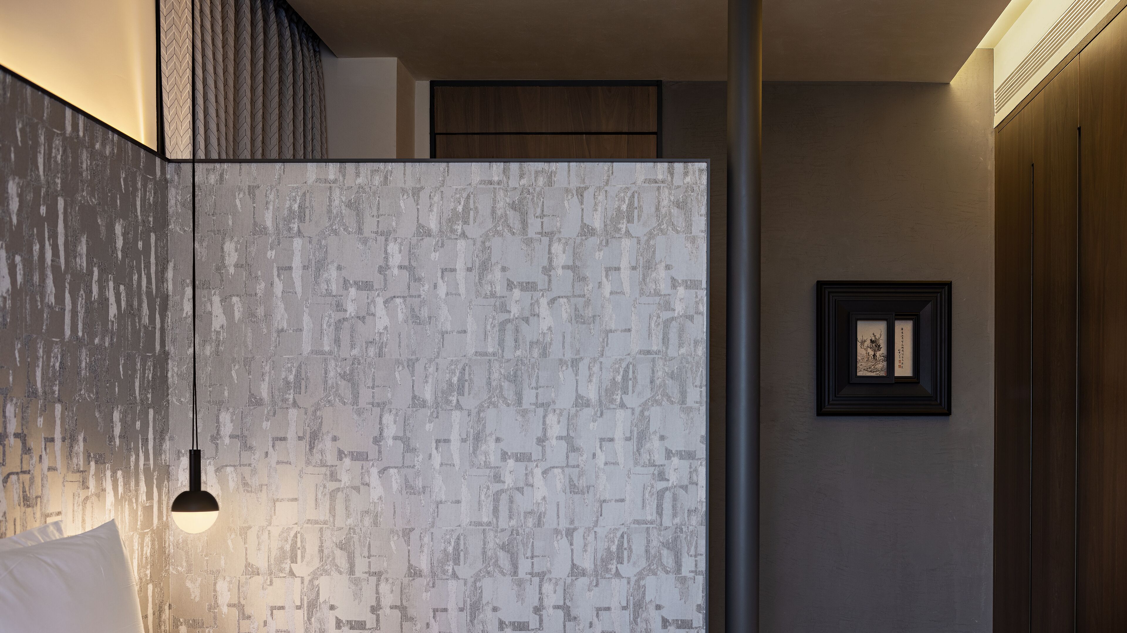 A modern interior with a textured wall, a hanging light fixture, and a framed artwork on the wall.