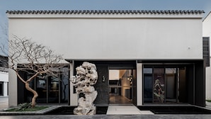 A modern building with a minimalist facade, large glass windows, and a distinctive rock sculpture in the entrance. - Jiangnan House Guanqianjie  (Suzhou)