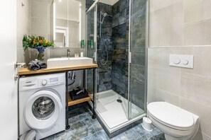 Une salle de bain moderne équipée d’un lave-linge, d’une cabine de douche et de toilettes.