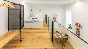 A modern bedroom with a bed, bedside tables, a glass railing, and a dining area with chairs and a table.