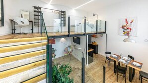 A modern interior with a staircase, a dining area, and a living space with a TV and artwork.