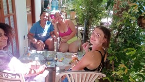 Een groep mensen zit aan een buitentafel met verschillende gerechten en drankjes, omringd door groen.