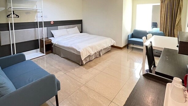 Quarto de hotel com uma cama, escrivaninha, poltrona, sofá e mesa pequena.