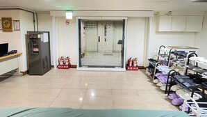 Um saguão de hotel com balcão de recepção, frigorífico, extintores de incêndio e um apoio para sapatos.